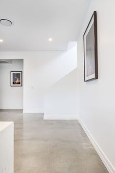 an empty room with white walls and concrete flooring, framed pictures on the wall