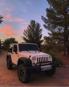 a white and black jeep parked on the side of a road at sunset with trees in the background