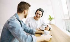 two men sitting at a table talking and drinking coffee