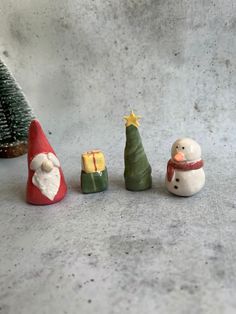 three small christmas trees are sitting next to each other on the ground, one with a snowman and another with a santa hat