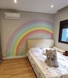 an elephant sitting on top of a bed next to a rainbow painted wall behind it