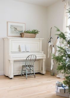 a white piano sitting in the corner of a room next to a small christmas tree