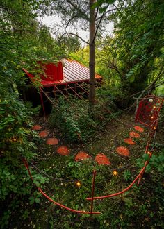 a red structure in the middle of some trees and bushes with lights on it's sides