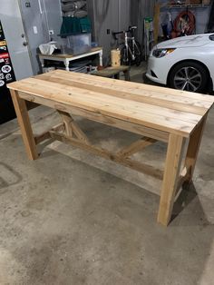 a wooden table sitting inside of a garage next to a white car in the background