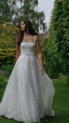 a woman in a white dress is walking through the grass with her hand on her hip