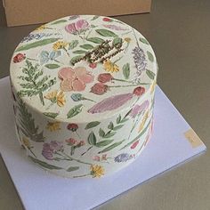 a white cake with flowers on it sitting on top of a blue napkin next to a box