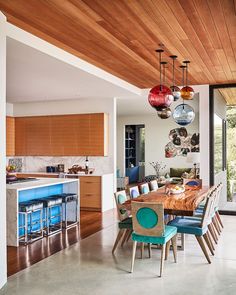 a dining room and kitchen area with wood ceilinging, blue chairs and wooden table