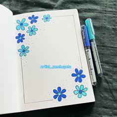 an open notebook with blue flowers on it and two pens sitting next to the book