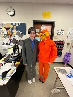 two men in orange suits standing next to each other near a desk with papers on it