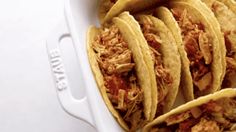 several tacos in a white casserole dish with shredded meat and sauce on top