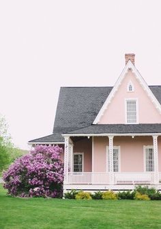 a pink house in the middle of a green field with purple flowers on either side