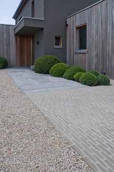 a house with gravel driveway next to it and bushes on the side of the road