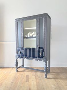 an old fashioned blue armoire with glass doors and drawers on the bottom, in front of a white wall