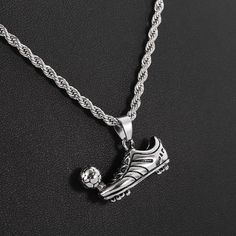 a silver necklace with a shoe and soccer ball hanging from the side on a black surface