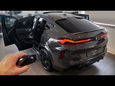 a person holding a mouse next to a gray sports car in a showroom with its door open