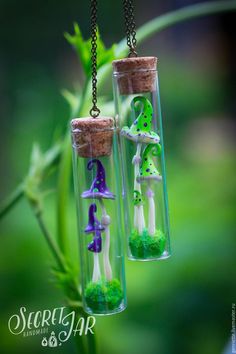 two glass bottles filled with tiny green and purple mushrooms hanging from chains on a tree branch