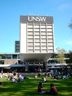 people sitting on the grass in front of a large building with an unsw sign above it