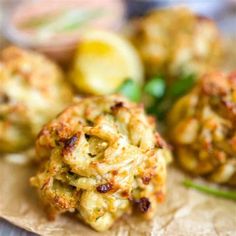 some crab cakes are sitting on a piece of parchment paper with lemons in the background