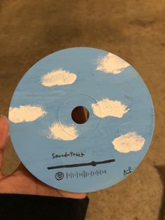 a hand holding a blue and white disc with clouds painted on it