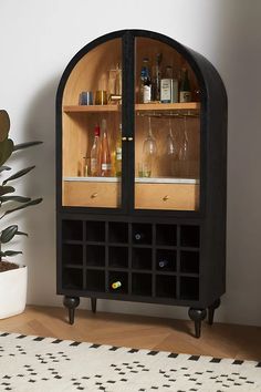 a black cabinet with wine glasses and liquor bottles on the top, in front of a potted plant