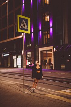 a woman standing next to a street sign on the side of a road at night