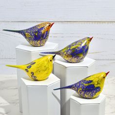 four yellow and blue birds sitting on white pedestals