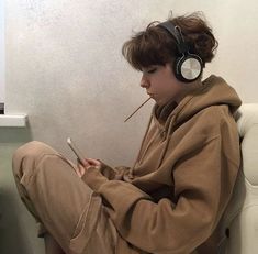 a boy sitting on the toilet with headphones on and looking at his cell phone