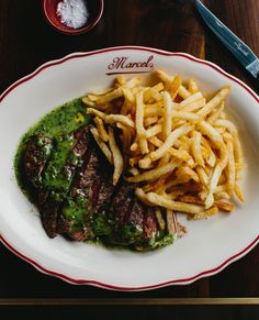 steak and french fries on a white plate with green sauce in front of the meal