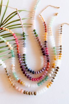 multicolored beaded necklaces with palm leaves on white background, top view