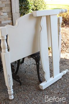 a white bed frame with black legs on graveled ground next to brick wall and bushes