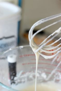 a whisk being poured into a glass bowl filled with milk and other ingredients