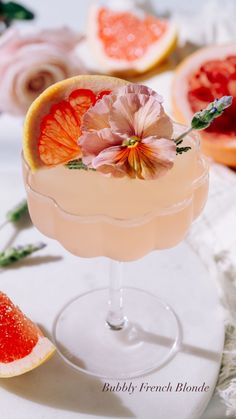 a glass filled with a drink and garnished with flowers next to slices of grapefruit