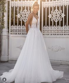 a woman standing in front of a white gate wearing a wedding dress with an open back