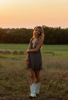 a woman standing in a field at sunset