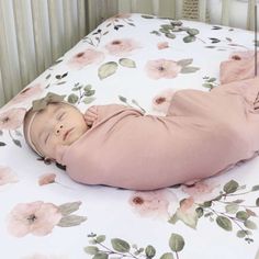 a baby laying on its back in a crib next to a wall with flowers