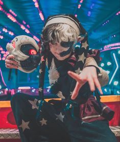 a young boy dressed up as a clown with his hands in the air while sitting down