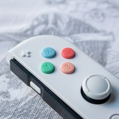 a video game controller sitting on top of a white table cloth with four colored buttons