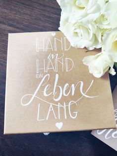 a brown box with white writing on it next to some flowers and a card that says hand - held en leben lang