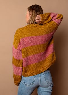 a woman in jeans and a sweater is standing against a wall with her back to the camera