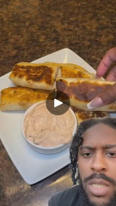 a man with dreadlocks is eating food on a plate and pointing to the camera