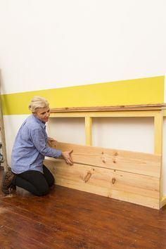 a woman kneeling on the floor next to a wooden bench with yellow painted walls behind it