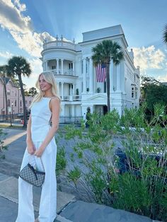 a woman standing on the sidewalk in front of a large white building with palm trees