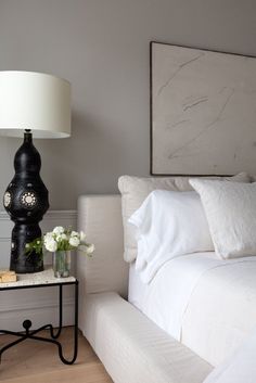 a bed with white sheets and pillows next to a table with a lamp on it