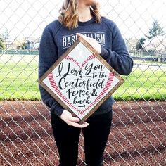 a woman holding up a baseball sign in front of a fence