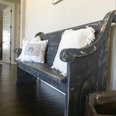 a wooden bench with pillows on it in front of a white wall and wood floor