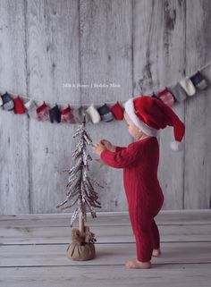 a baby in a santa hat is playing with a small christmas tree on a wooden floor