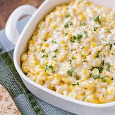 a casserole dish with corn and cheese in it on a blue towel next to a wooden spoon