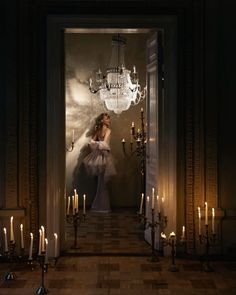 a woman in a white dress standing at the entrance to a room with candles and chandeliers