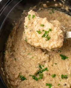 a ladle full of mashed potatoes and parsley in a slow cooker