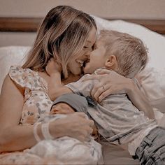 a woman laying in bed with a little boy on her lap and kissing her cheek